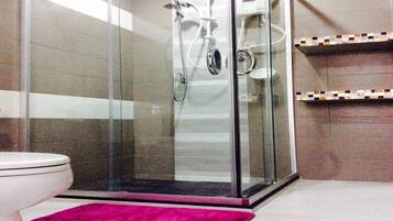 A bathroom with a glass-enclosed shower, a toilet, and tiled walls.