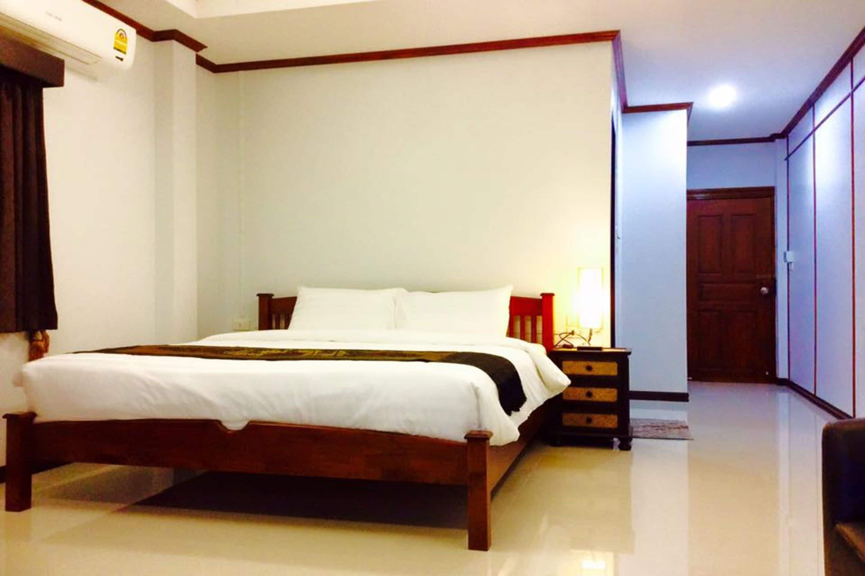 Un dormitorio con cama de madera, ropa de cama blanca, una mesita de noche con lámpara y un armario.