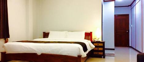 Un dormitorio con cama de madera, ropa de cama blanca, una mesita de noche con lámpara y un armario.