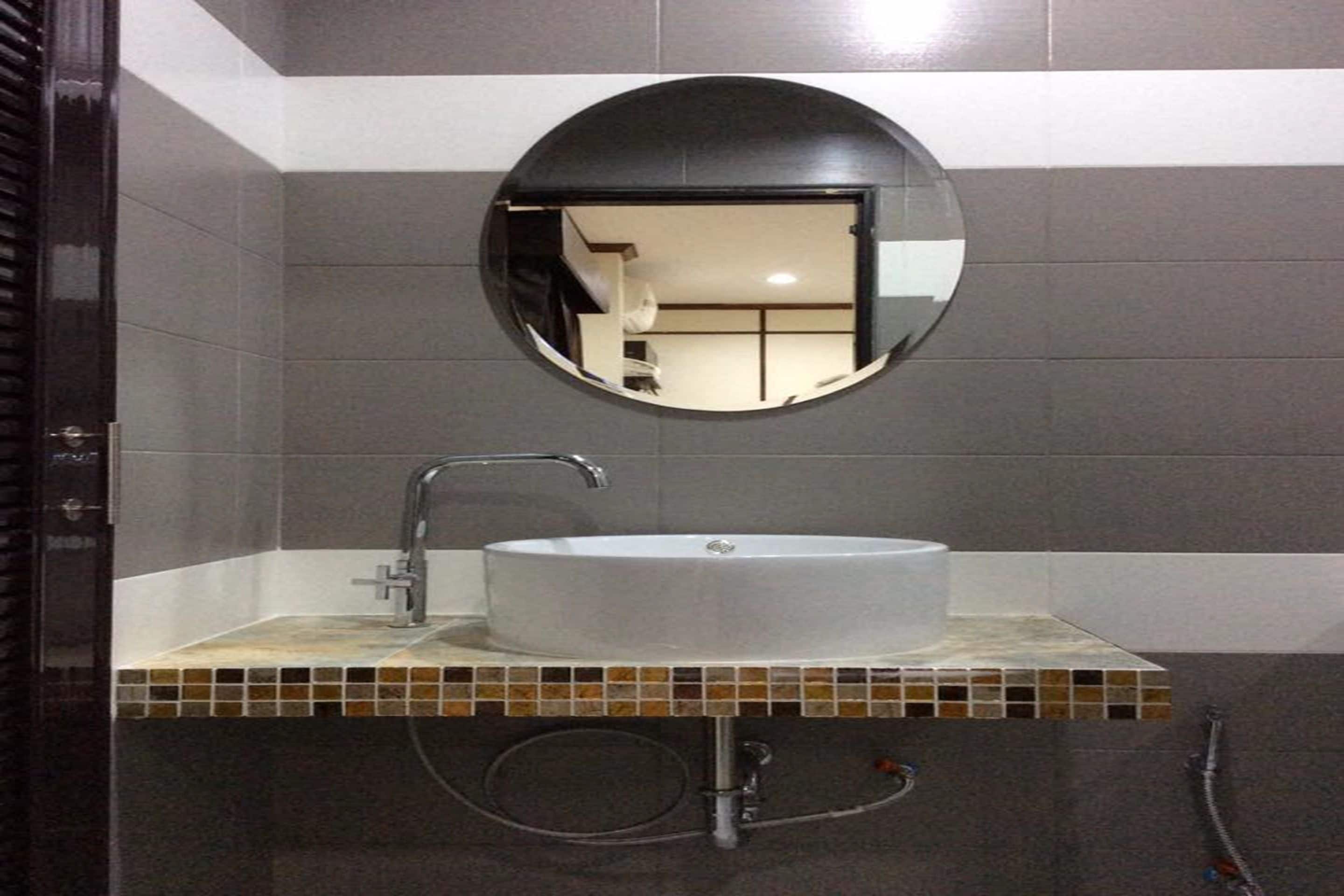 A bathroom with a round mirror, a white sink, and a tiled backsplash.