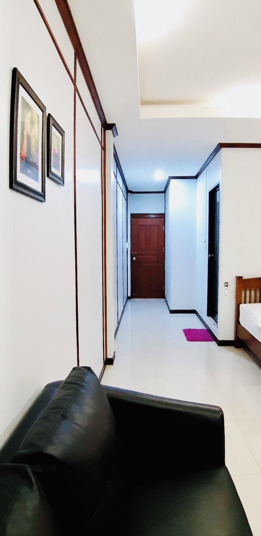 A hallway with a black leather sofa, a wooden door, and a bed with a white mattress.