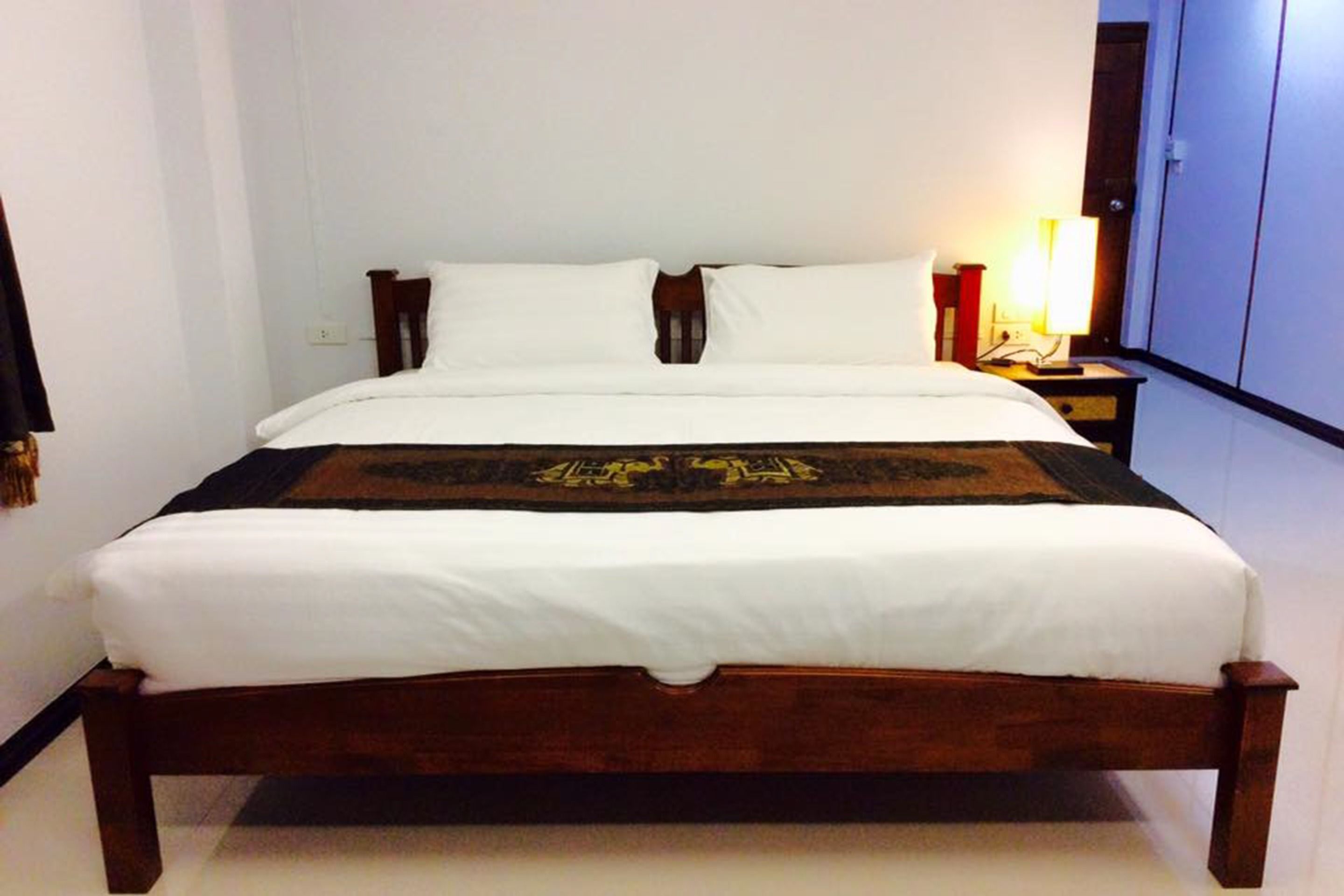 A standard hotel room with a wooden bed, white bedding, and a nightstand with a lamp.