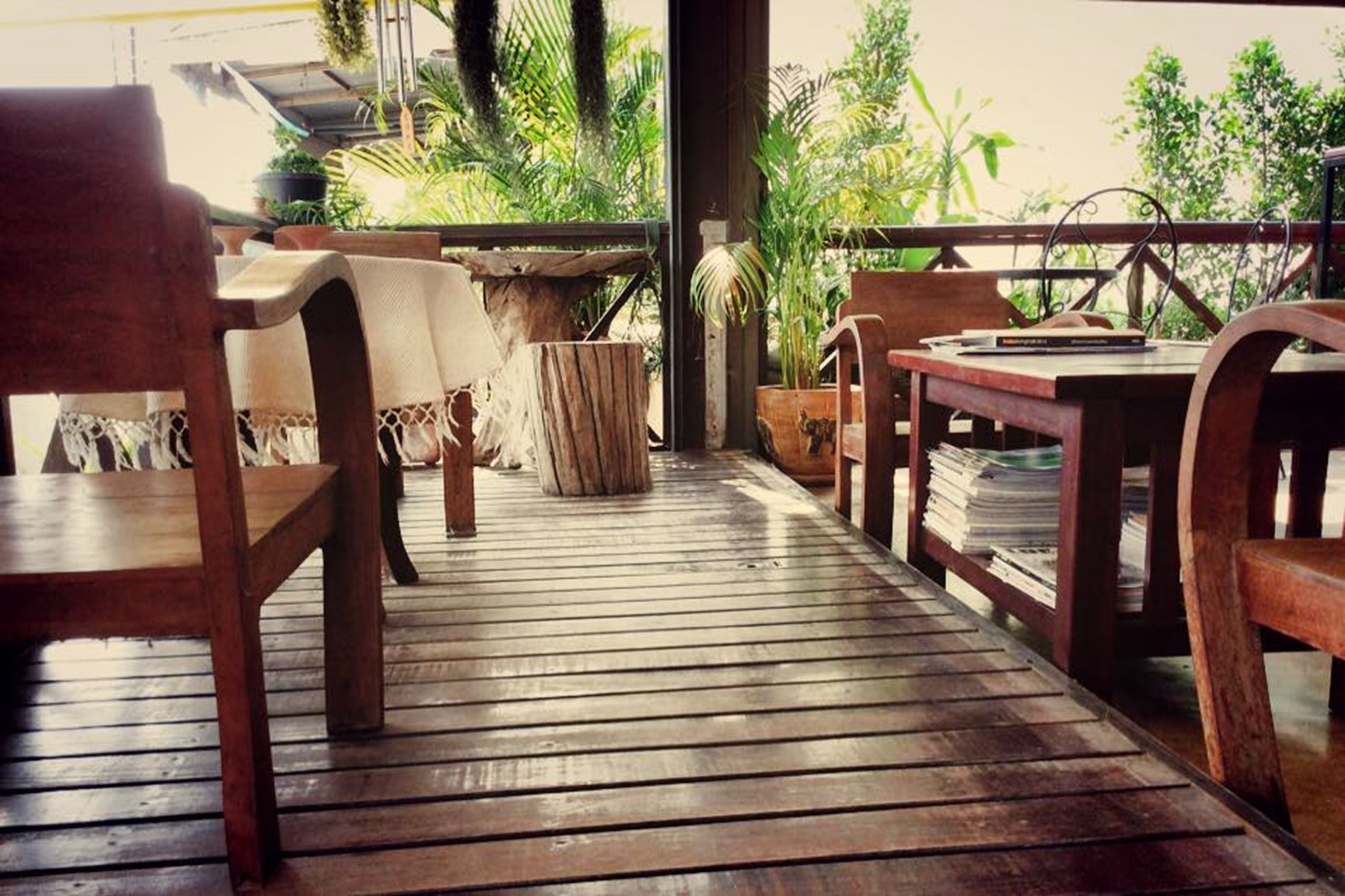 A wooden deck with tables and chairs, surrounded by lush greenery.
