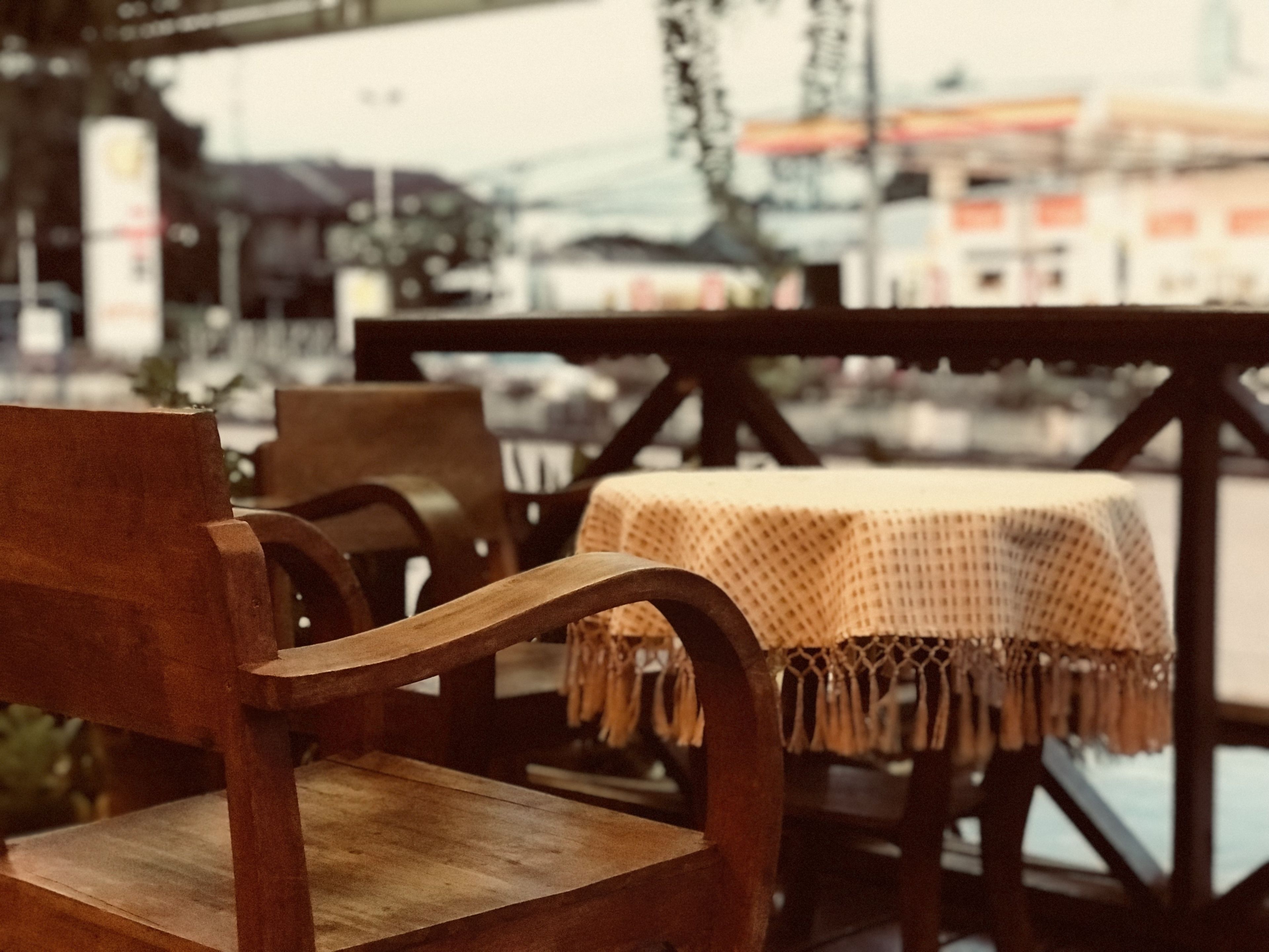 A wooden chair and table set on an outdoor balcony with a view of buildings and a bridge in the background.