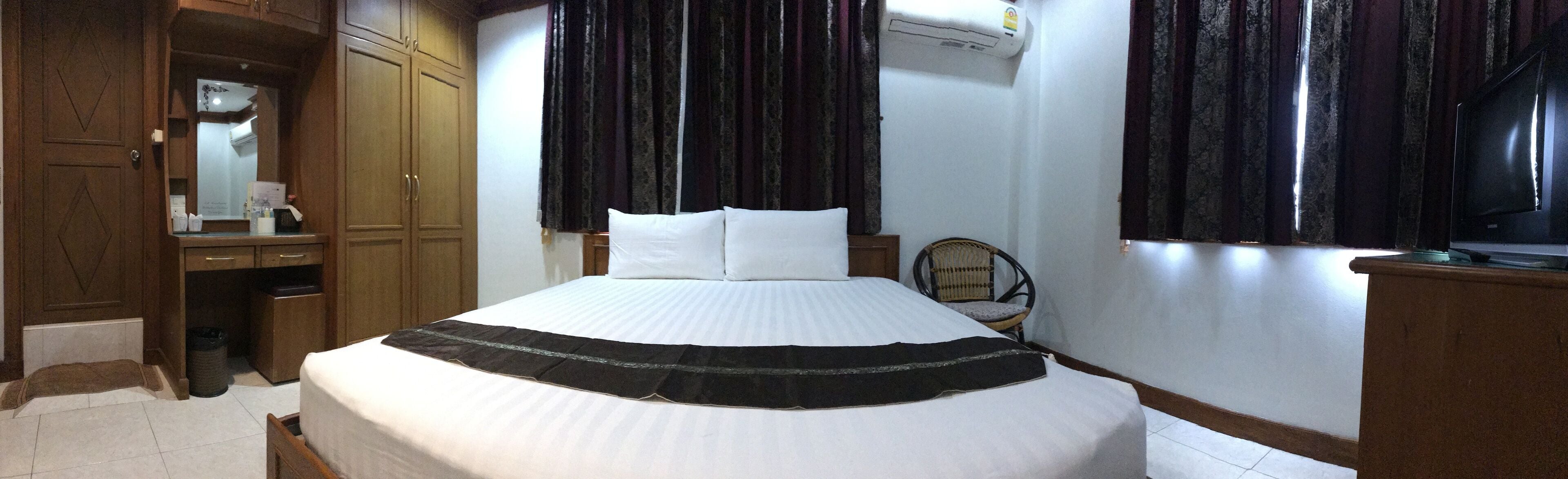 A hotel room with a large bed, a wardrobe, a chair, and a television.