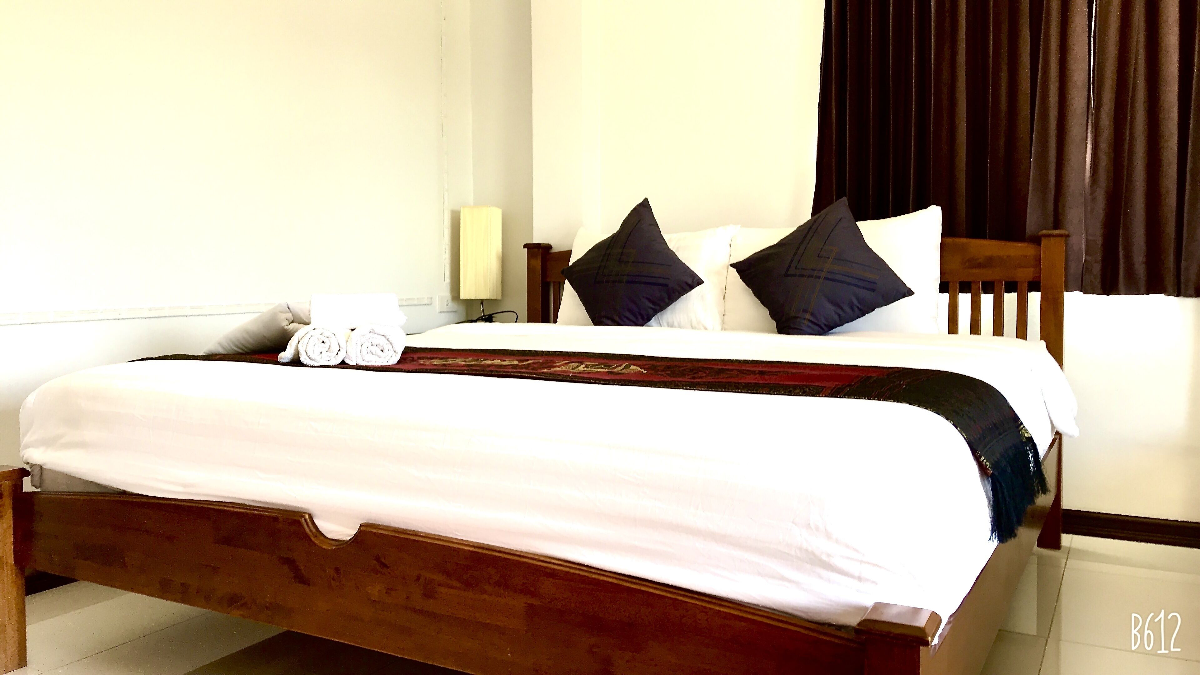 Una cama bien hecha con sábanas blancas y toallas enrolladas, cabecera de madera y almohadas oscuras.