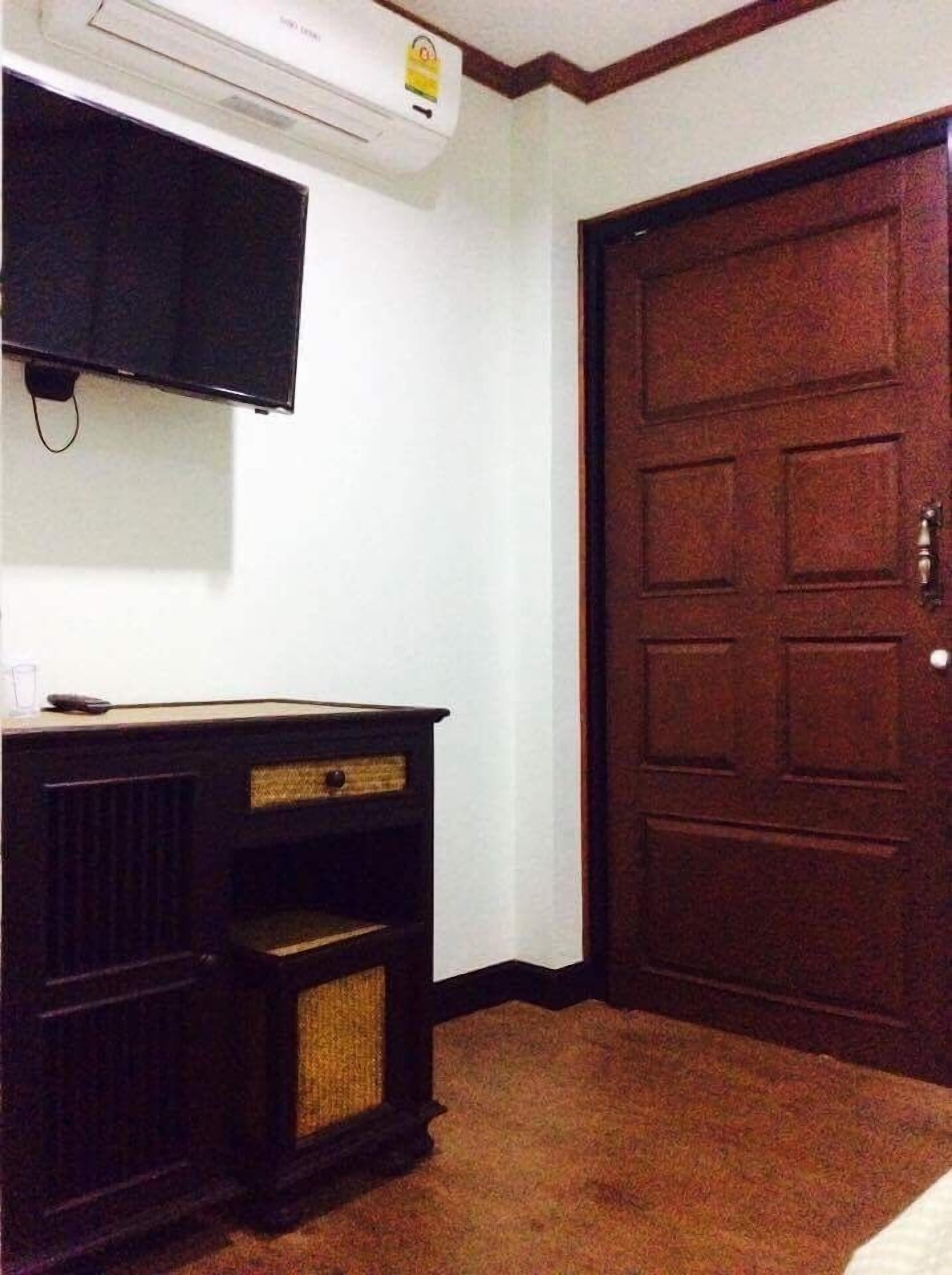 A room with a dark wooden dresser, a flat-screen TV mounted above it, and a large wooden door.