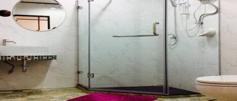 A bathroom with a glass shower enclosure, a round mirror, a sink, and a toilet.