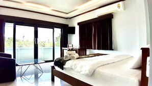 A hotel room with a bed, a small table, a chair, and a balcony with a view. - EZ House & Cafe (Sukhothai)