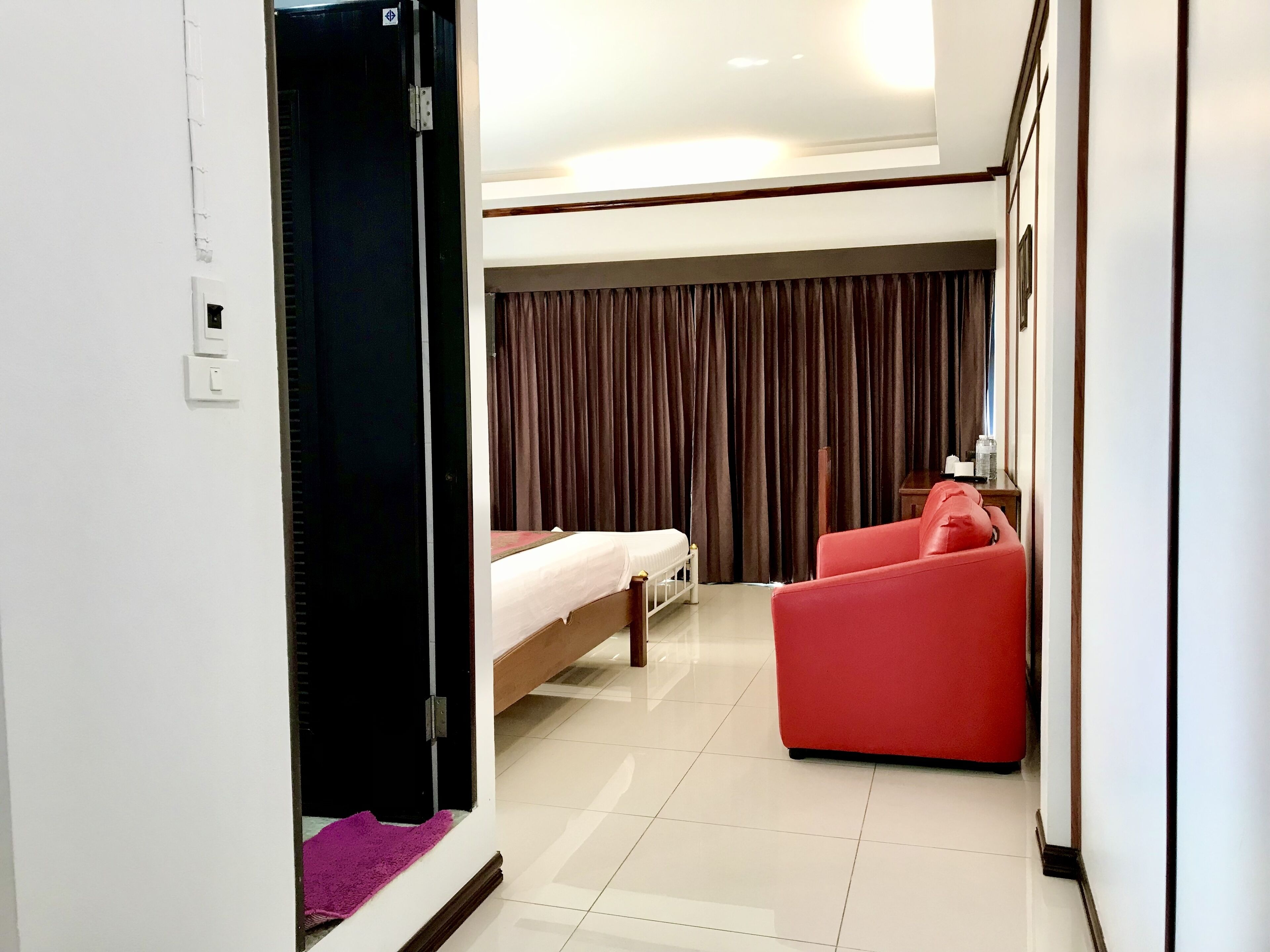 Habitación de hotel con una cama, un sofá rojo, una mesita y una cortina.