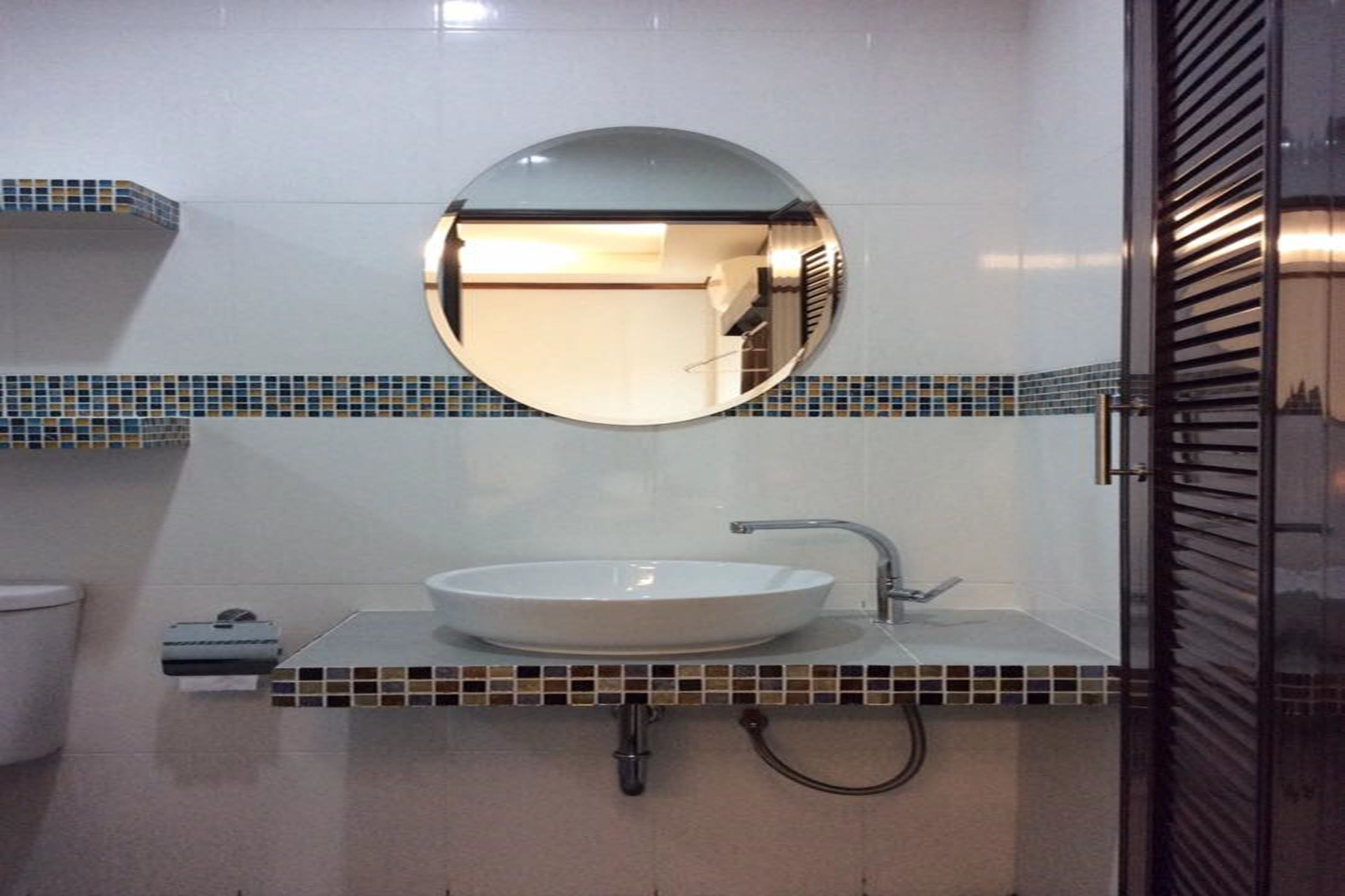 A bathroom with a round mirror, a white sink, and a tiled backsplash.