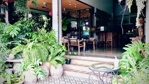A restaurant with outdoor seating, potted plants, and a glass door entrance. - EZ House & Cafe (Sukhothai)