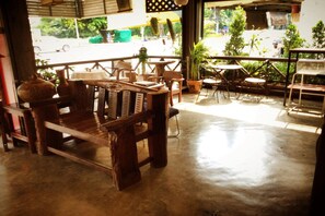 Un banco y mesas de madera rústica en un café, con vista a la calle y zonas verdes.
