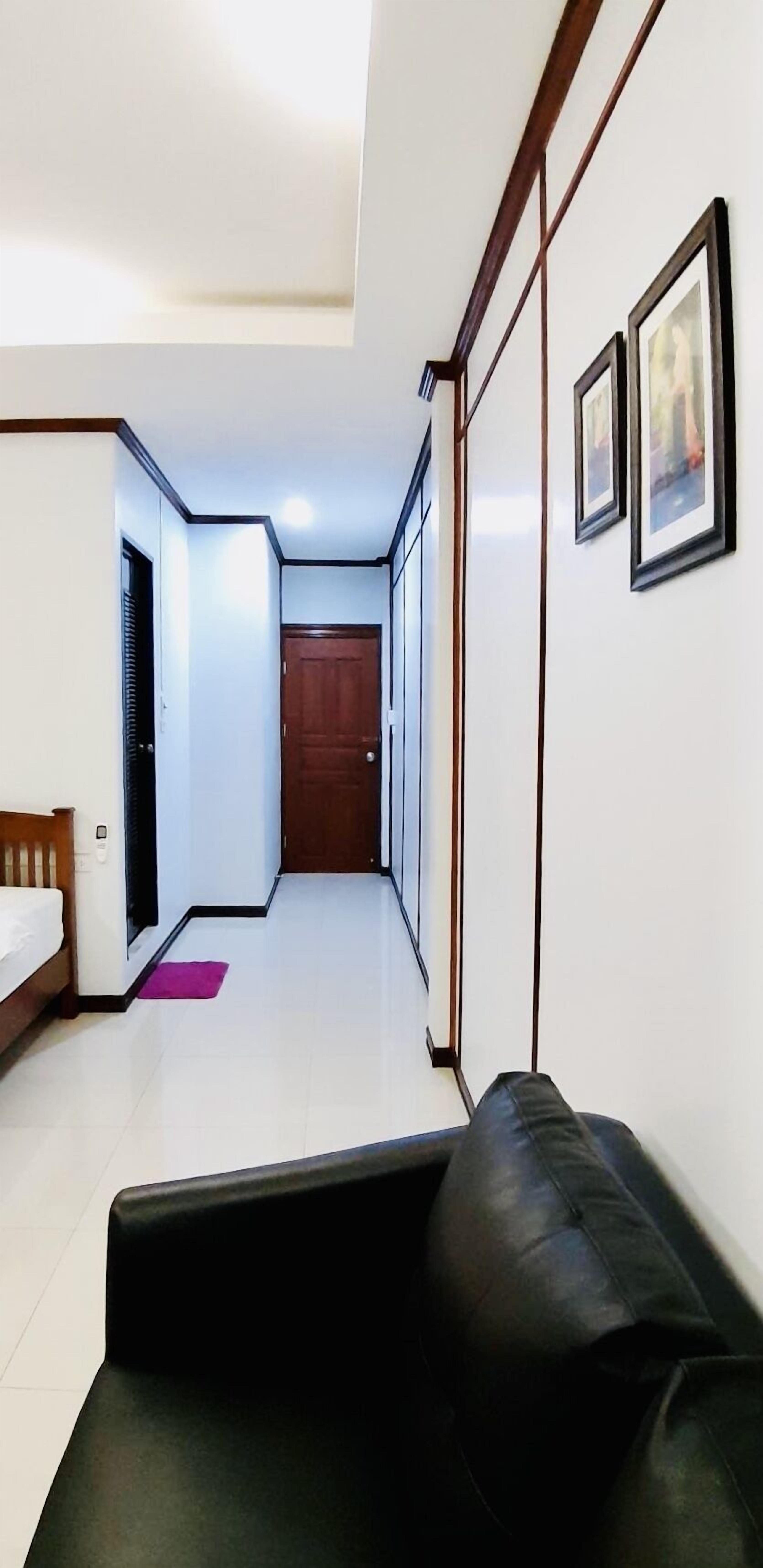 Un couloir étroit avec un canapé en cuir noir, une porte en bois et des tableaux encadrés accrochés au mur.
