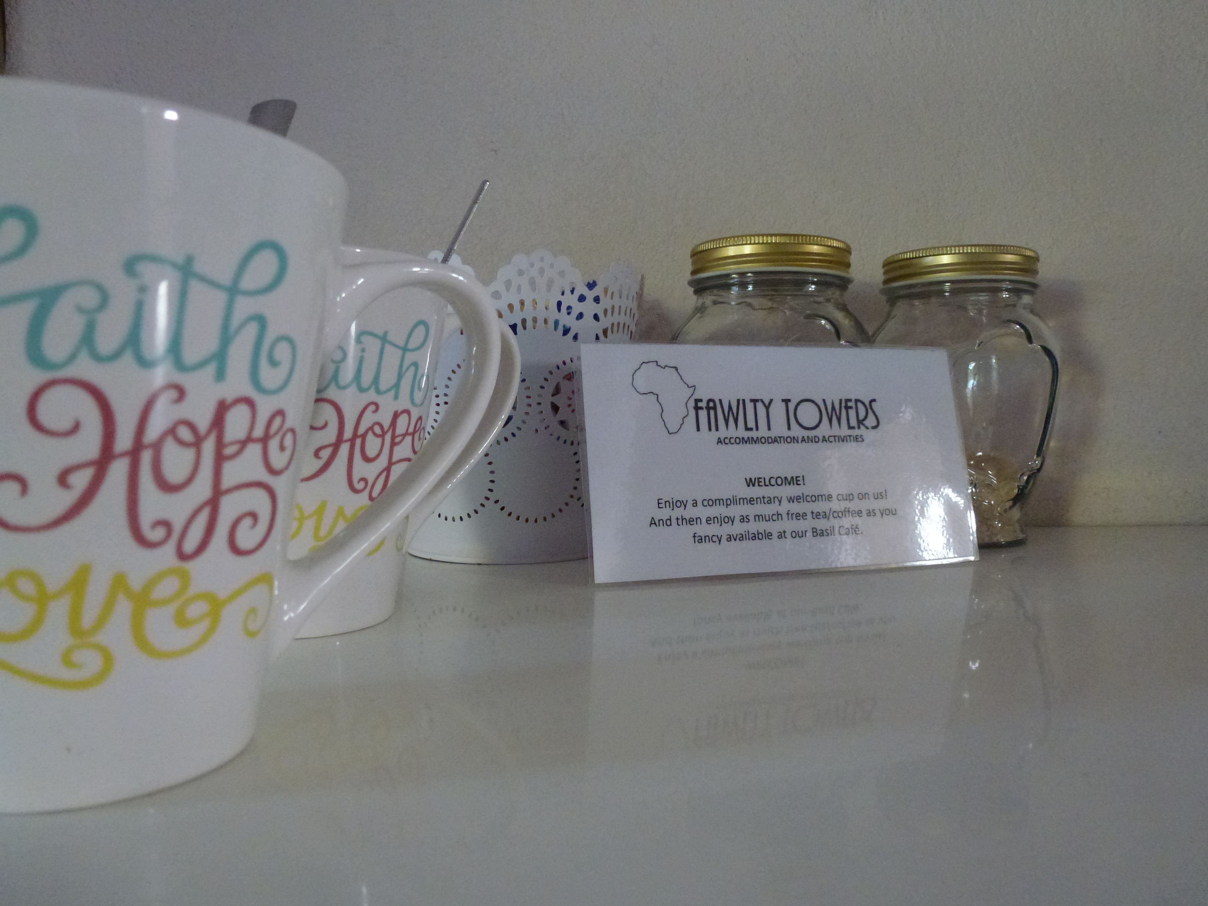 Una exhibición de tazas de cerámica con frases motivadoras, un letrero de Fawly Towers y dos frascos de vidrio con tapas doradas.