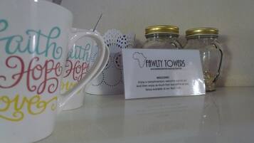 Una exhibición de tazas de cerámica con frases motivadoras, un letrero de Fawly Towers y dos frascos de vidrio con tapas doradas.
