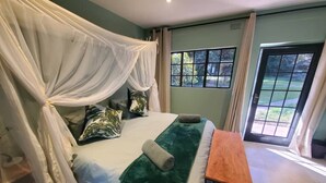 A bedroom with a bed, a bench, a window, and a door. - Fawlty Towers Guest House (Livingstone)