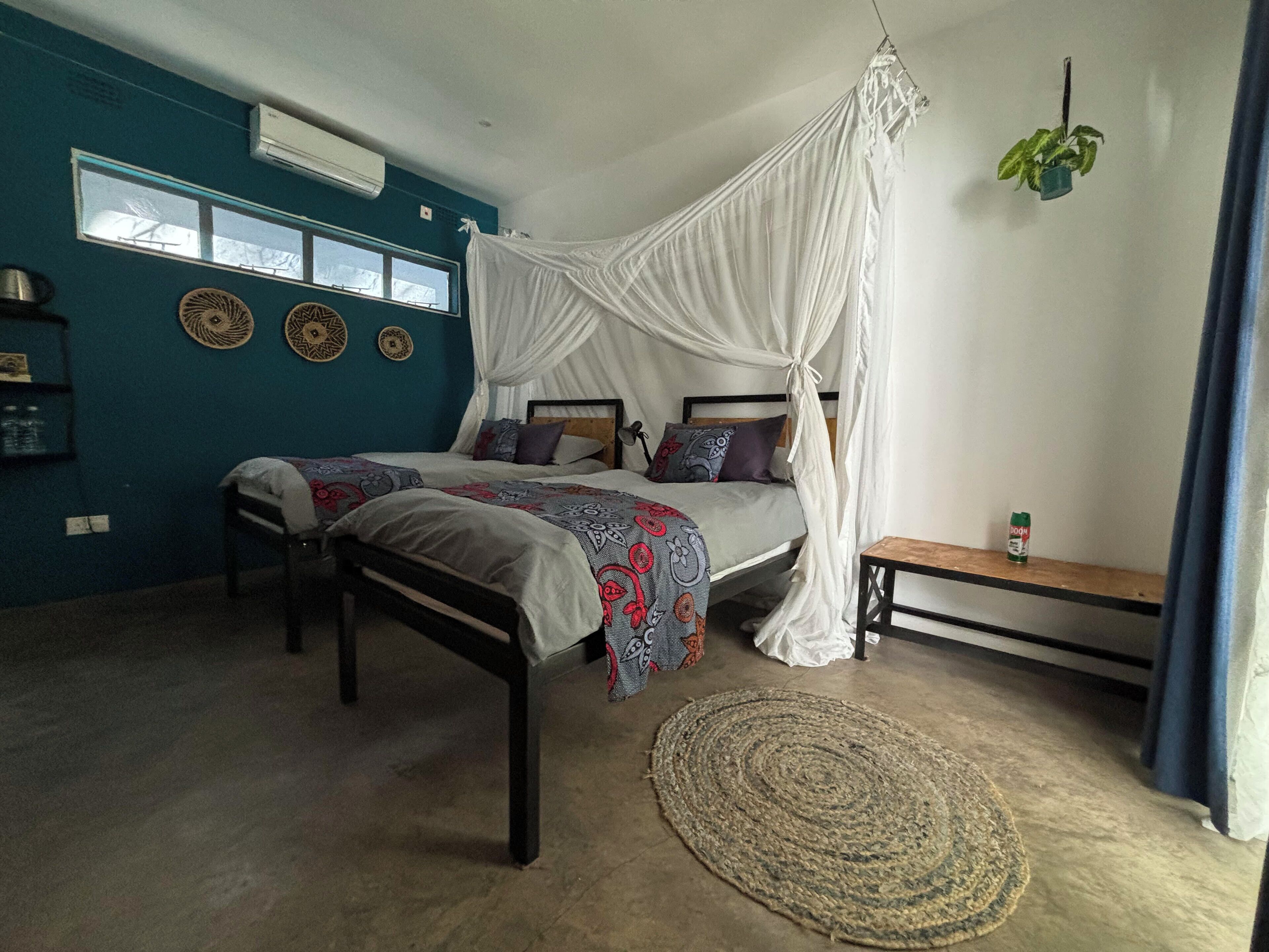 A bedroom with a canopy bed, a small bedside table, a potted plant, and decorative wall plates.