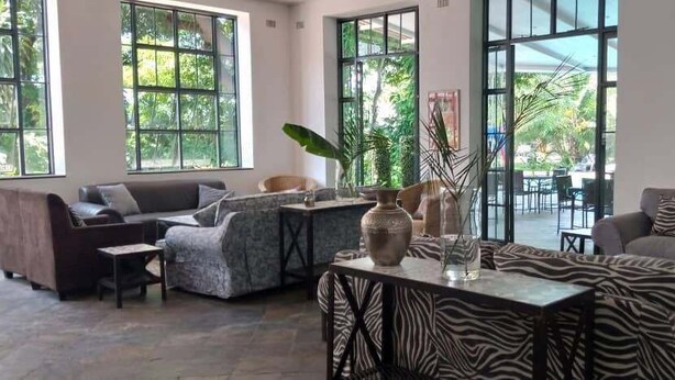 A spacious living area with large windows, a sofa set, a coffee table, and decorative vases. - Fawlty Towers Guest House (Livingstone)