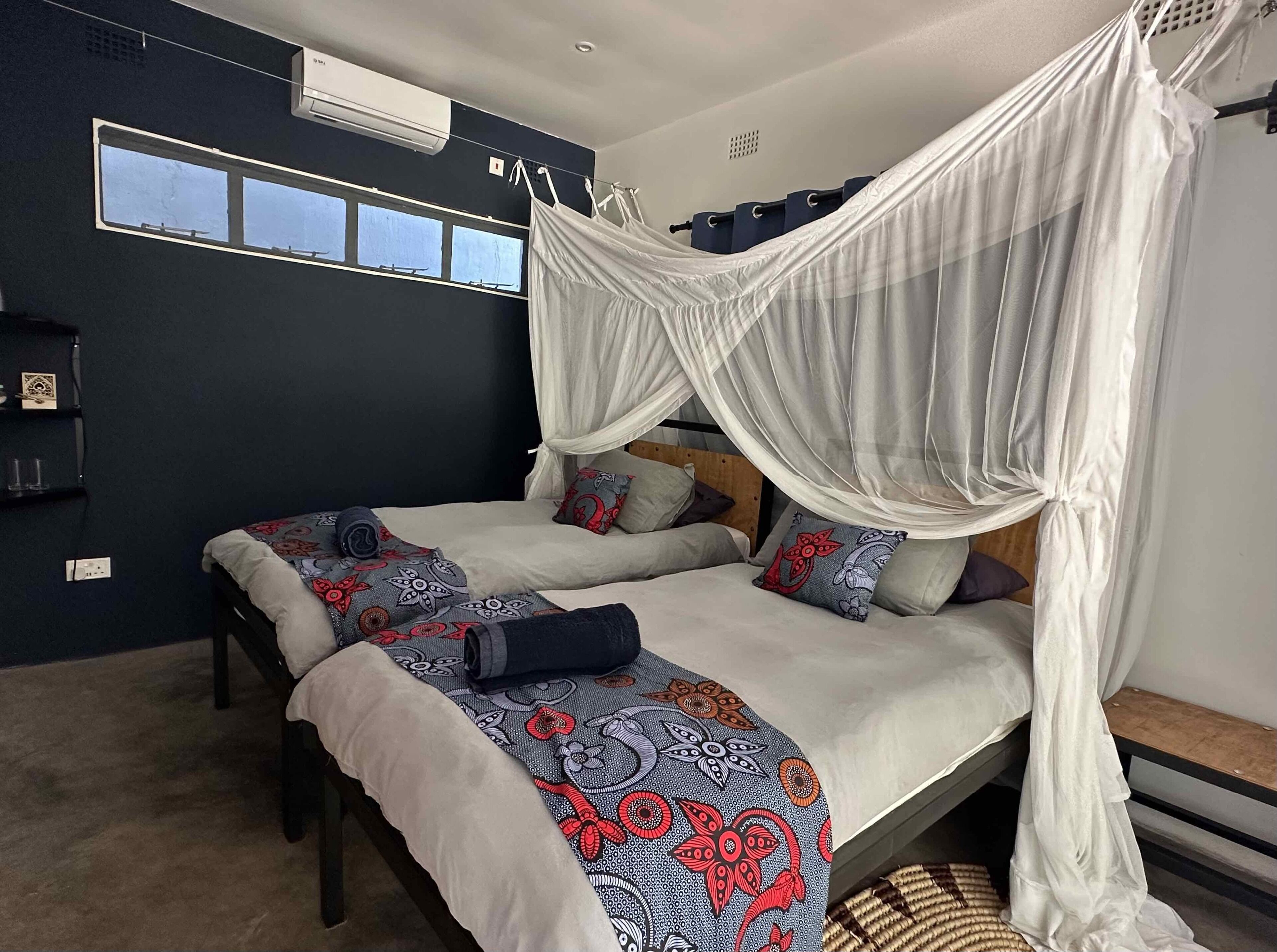 A bedroom with two beds, each with a canopy, a window, and a shelf with items.