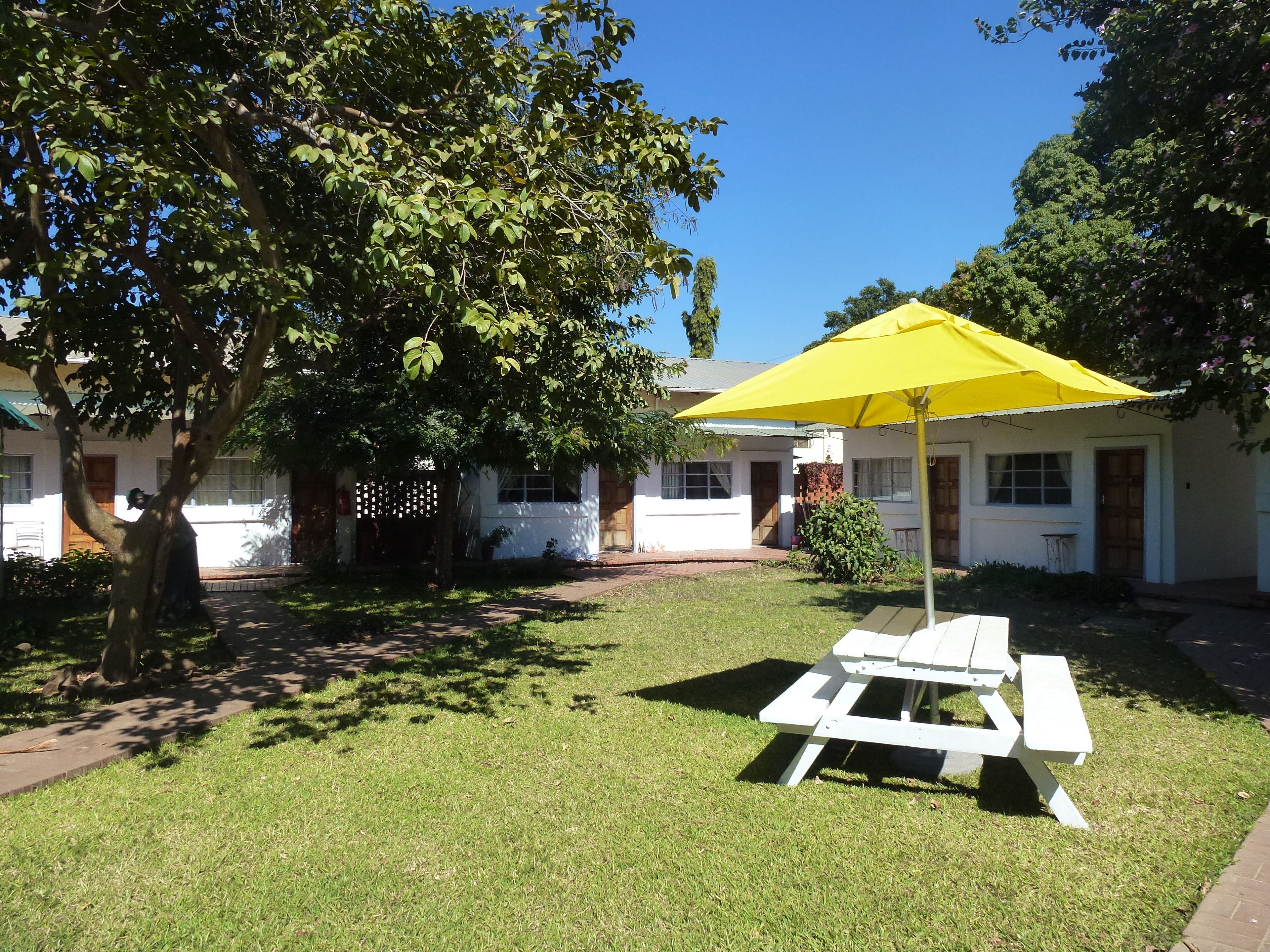 A grassy outdoor area with a white picnic table and a yellow umbrella.