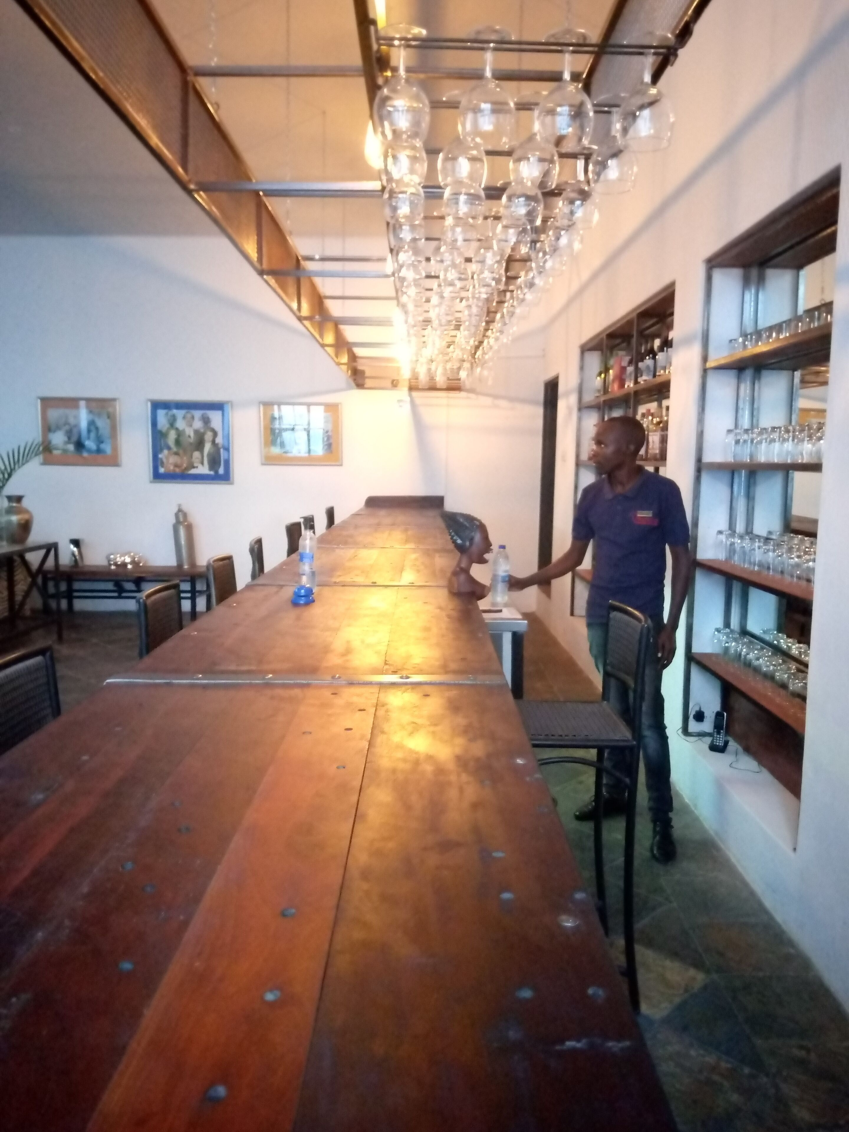 Una larga mesa de madera con sillas, una araña y estantes con cristalería.