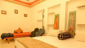 A room with two beds, a sofa, and a chair. There are framed pictures on the walls. - Hotel Hanuman Ghat (Udaipur)