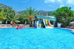 A swimming pool with a water slide, lounge chairs, and palm trees.