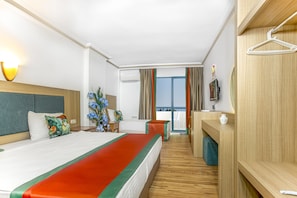 A hotel room with a large bed, a desk, a chair, a TV, and a balcony with curtains.
