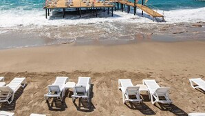 Een strand met witte ligbedden en een houten pier met vlaggen.
