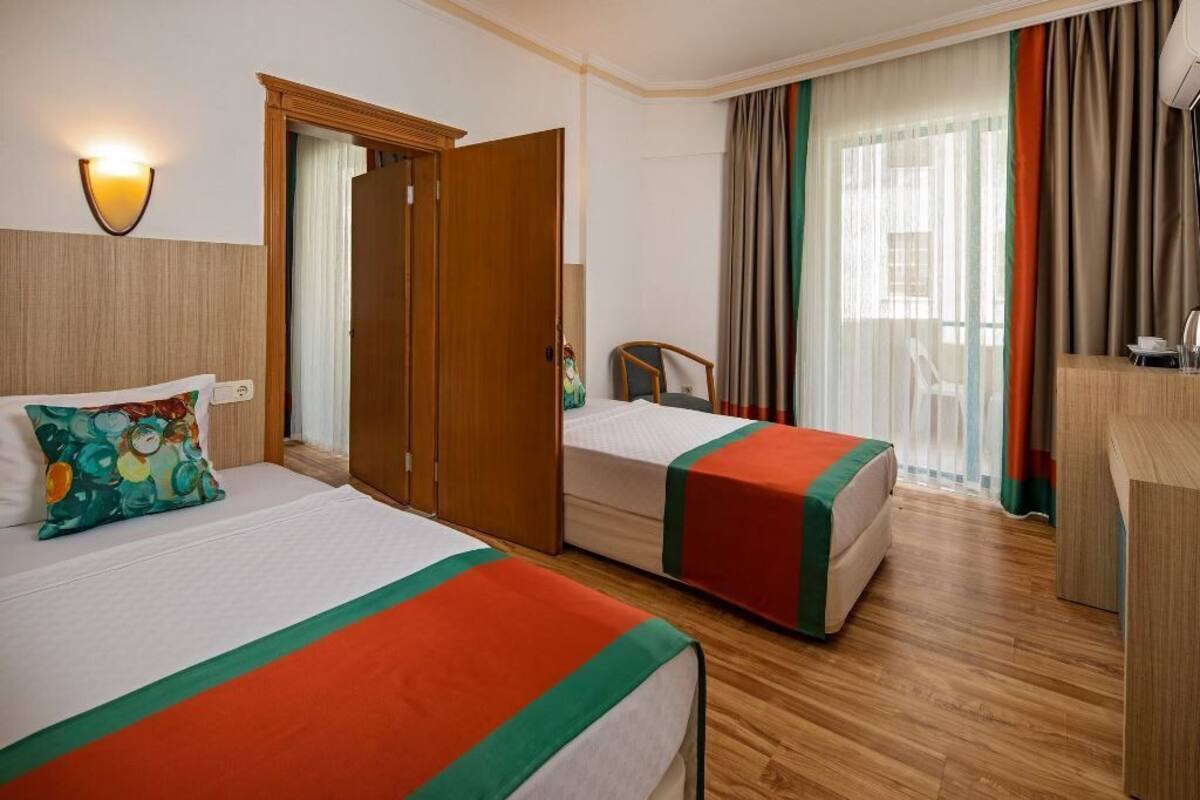 A hotel room with two beds, a wooden wardrobe, a desk, and a chair.