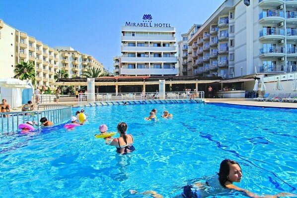 A swimming pool at Mirabel Hotel with multiple levels of balconies and a clear sky.