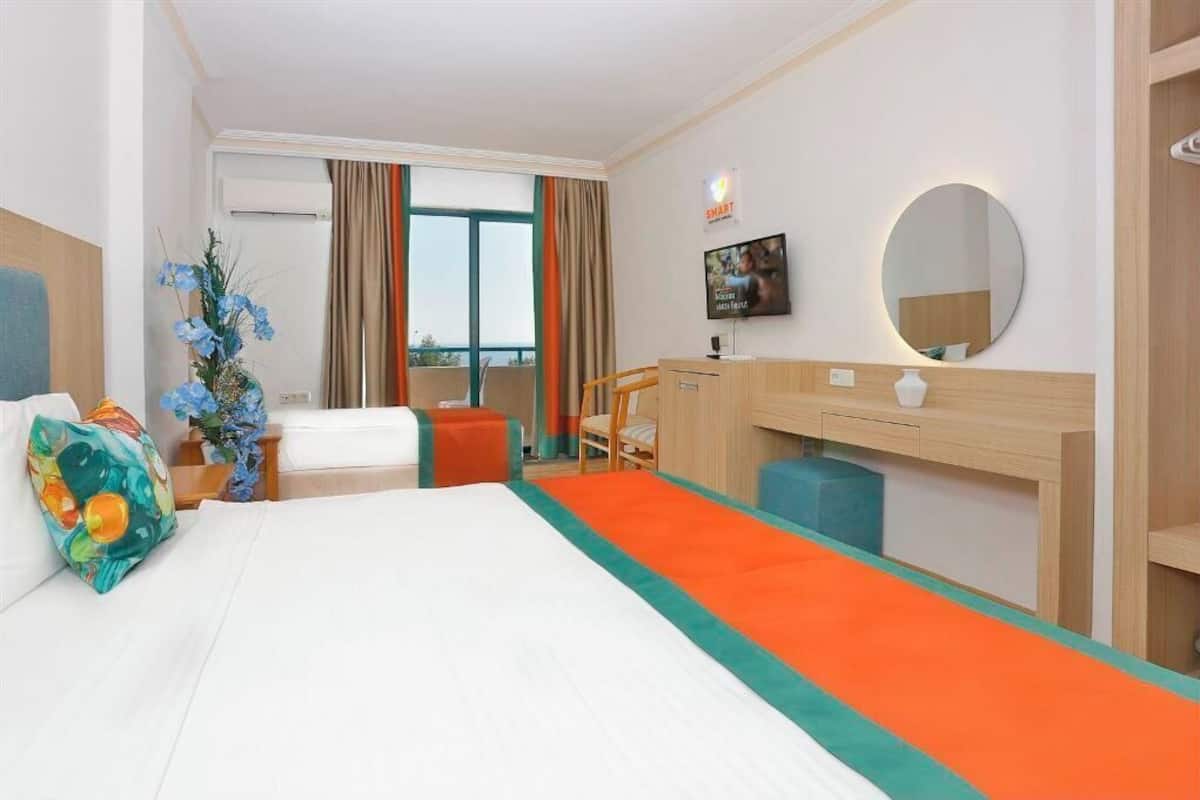 A hotel room with a bed, a desk, a chair, a TV, and a window with curtains.