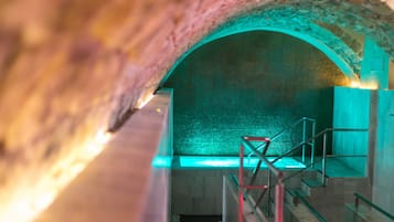 Een gewelfde tunnel met een betegelde muur en een metalen trap die naar beneden leidt.