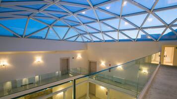 Un interior de hotel moderno con un atrio de cristal, varios pisos y un diseño geométrico en el techo.
