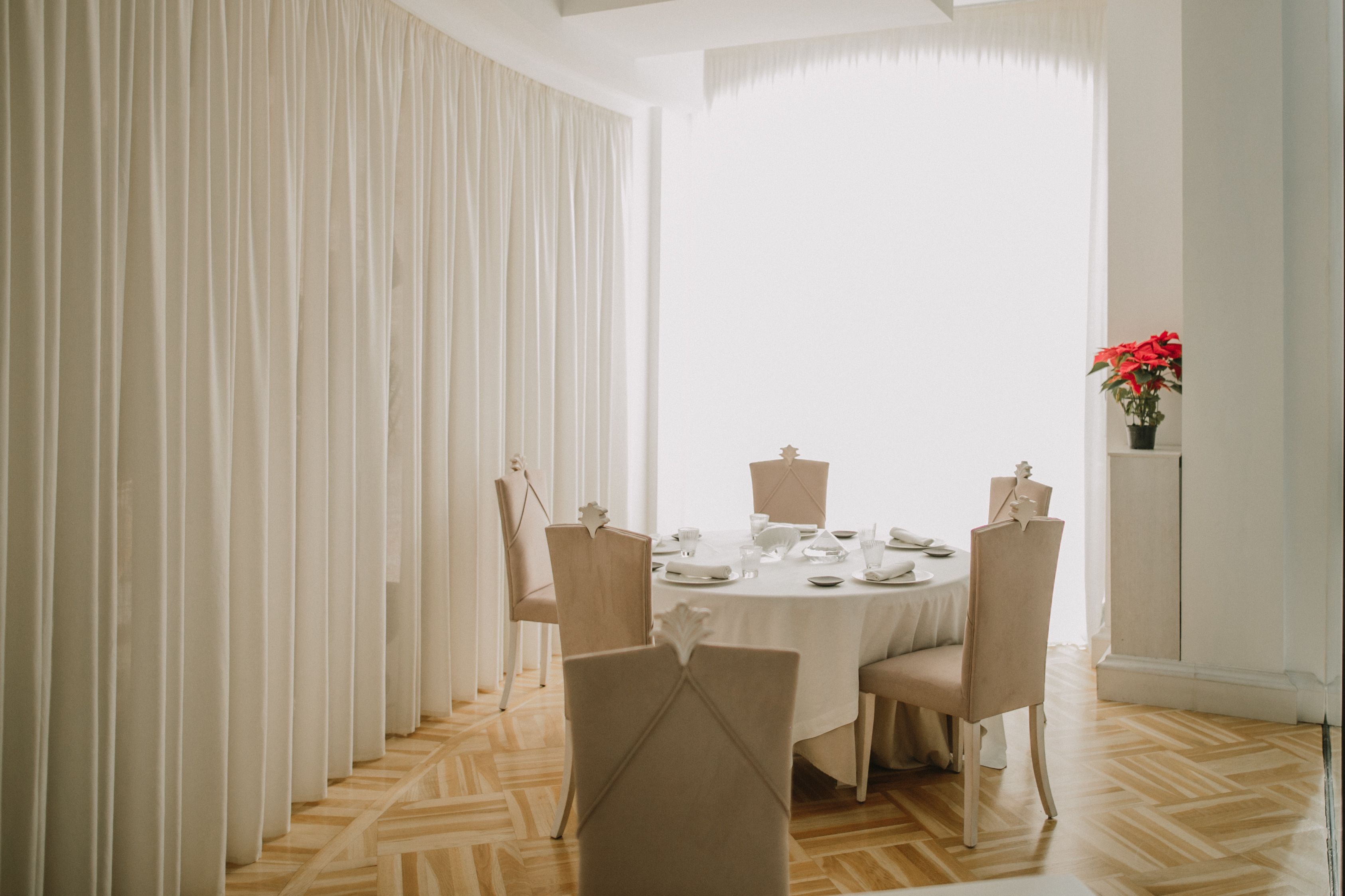 A dining area with a round table set for four, surrounded by chairs, with a potted plant on a cabinet to the right.