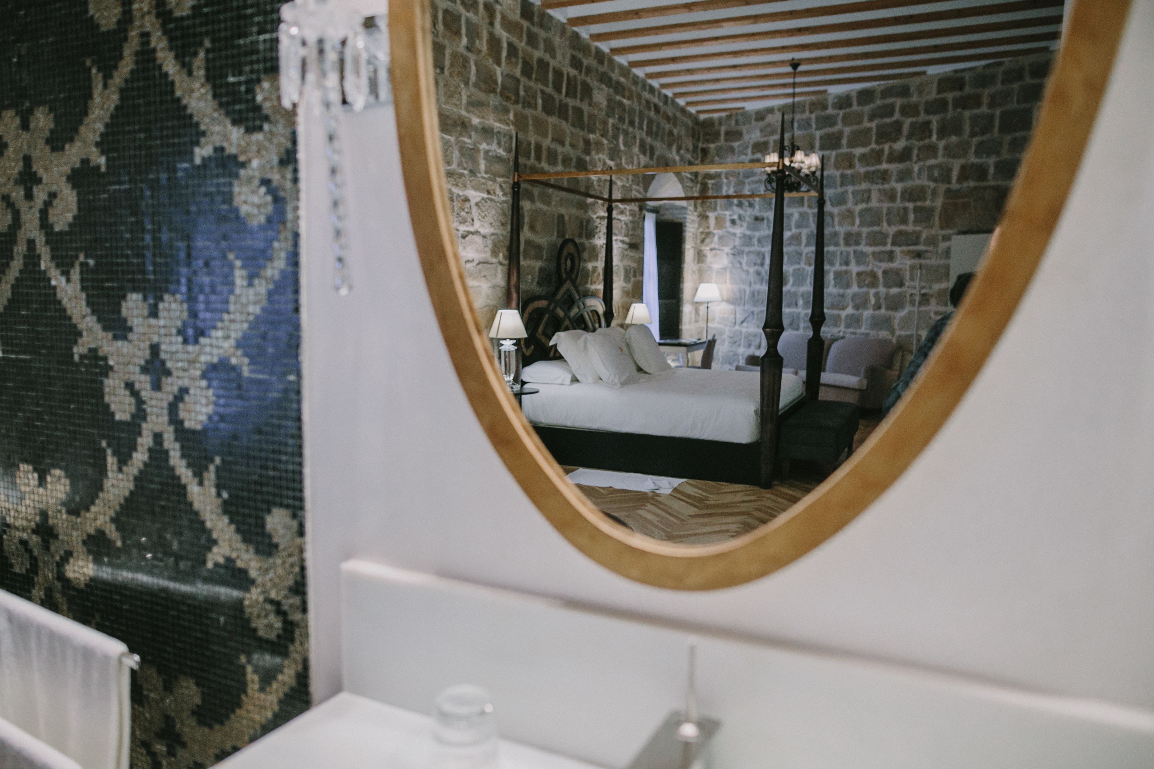 Un dormitorio con cama con dosel, un espejo grande y una pared de piedra.