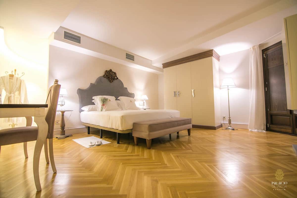 Una habitación de hotel con cama, mesitas de noche, una silla, armario y lámpara de pie.