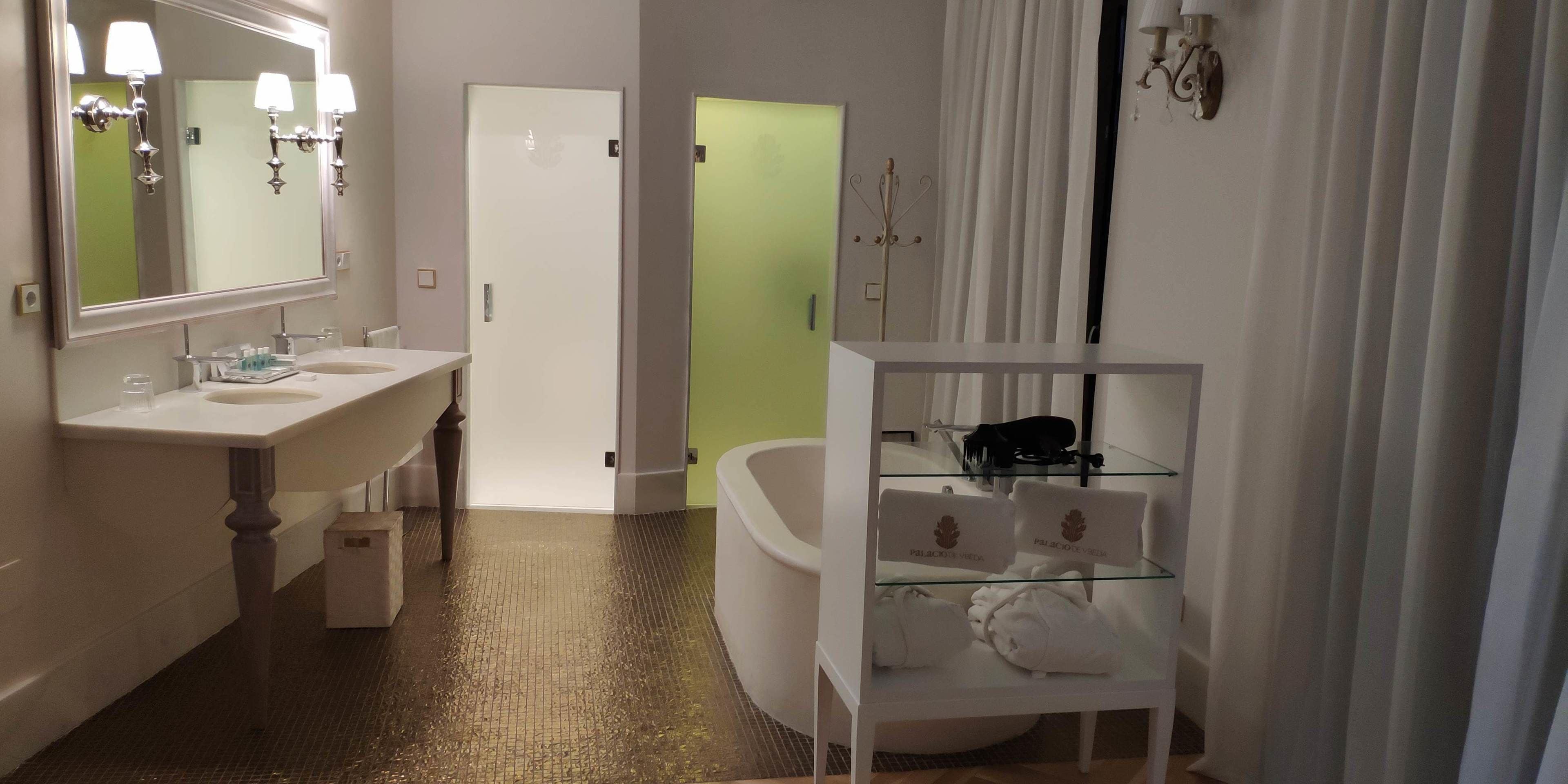 A modern bathroom with a large mirror, two sinks, a glass-topped vanity, a bathtub, and a glass shelf with towels.