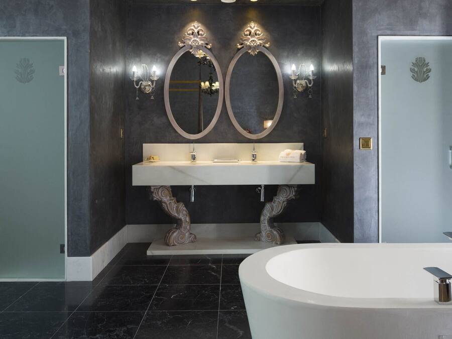Un baño moderno con dos puertas, una bañera independiente grande y un tocador con espejo y apliques.