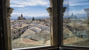 A view through an arched window of a historic town with buildings and a distant mountain range.