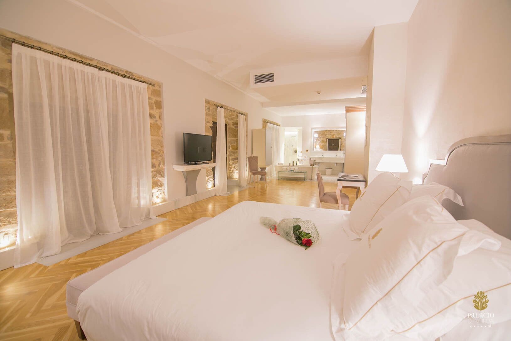 A hotel room with a large bed, a television, a desk, and a bathroom visible through an open door.