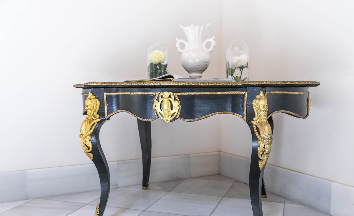 Una mesa en esquina con diseño negro y dorado, que incluye un florero y un recipiente de vidrio con flores.