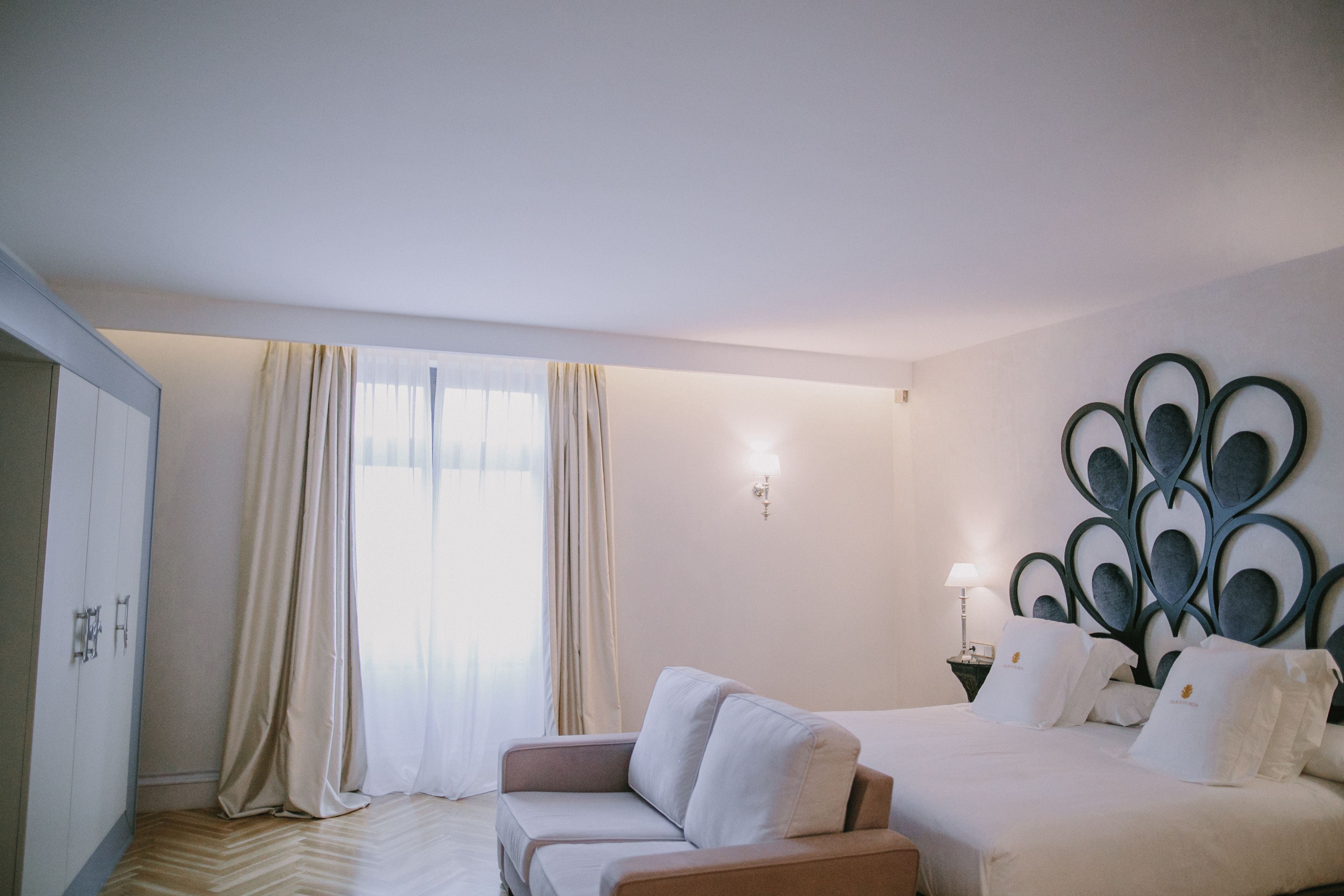 A hotel room with a bed, a sofa, a wardrobe, and a decorative wall piece.
