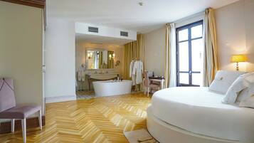 Habitación de hotel con una cama grande, zona de estar con una silla, escritorio, bañera y un ventanal con cortinas.