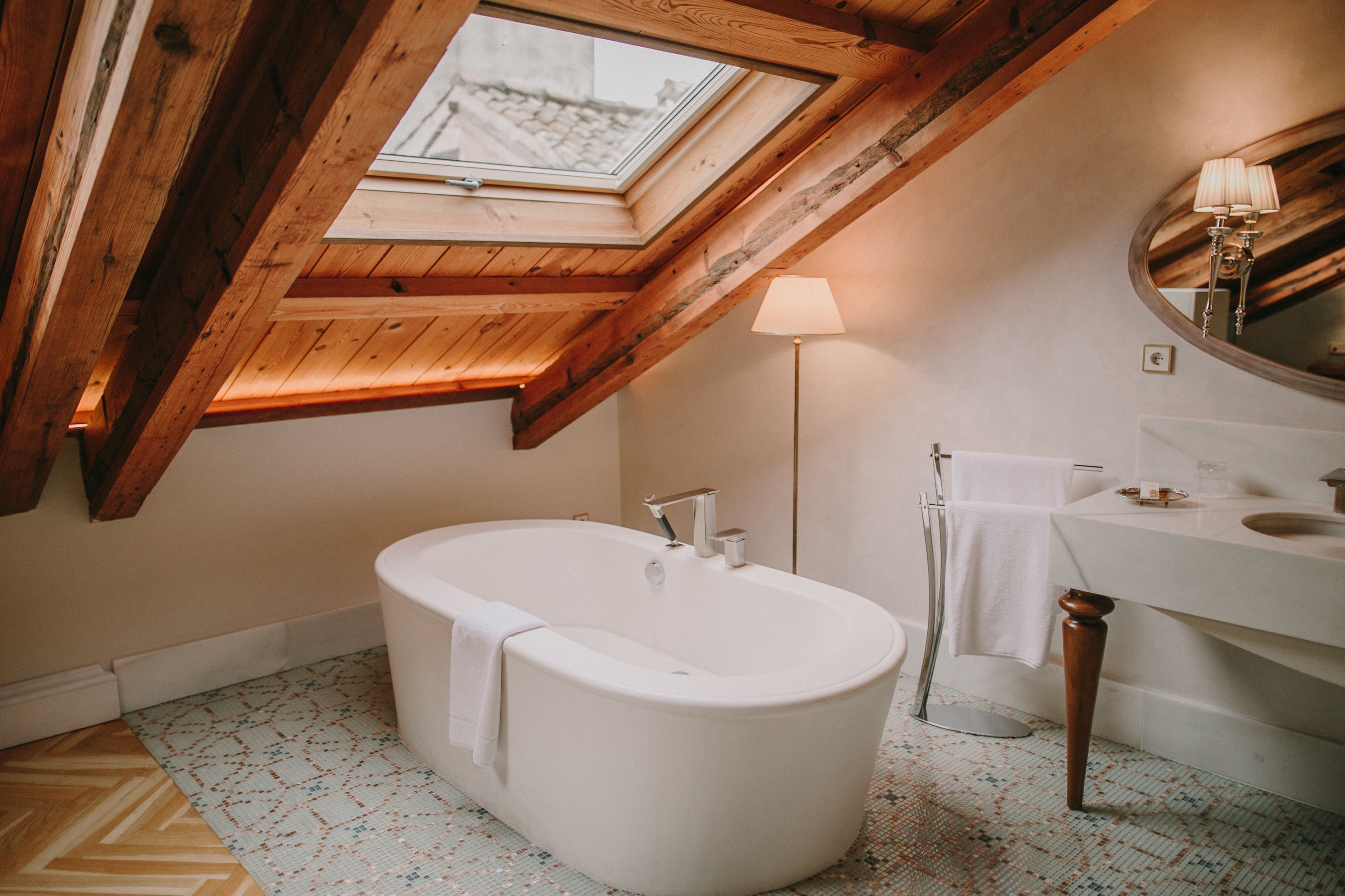 Un baño moderno con tragaluz, una bañera independiente, un tocador con espejo y un suelo de diseño geométrico.