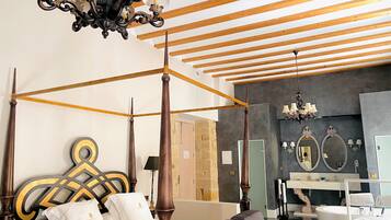 Una cama con dosel, cabecera de madera, candelabro y un baño moderno con un espejo grande y bañera.