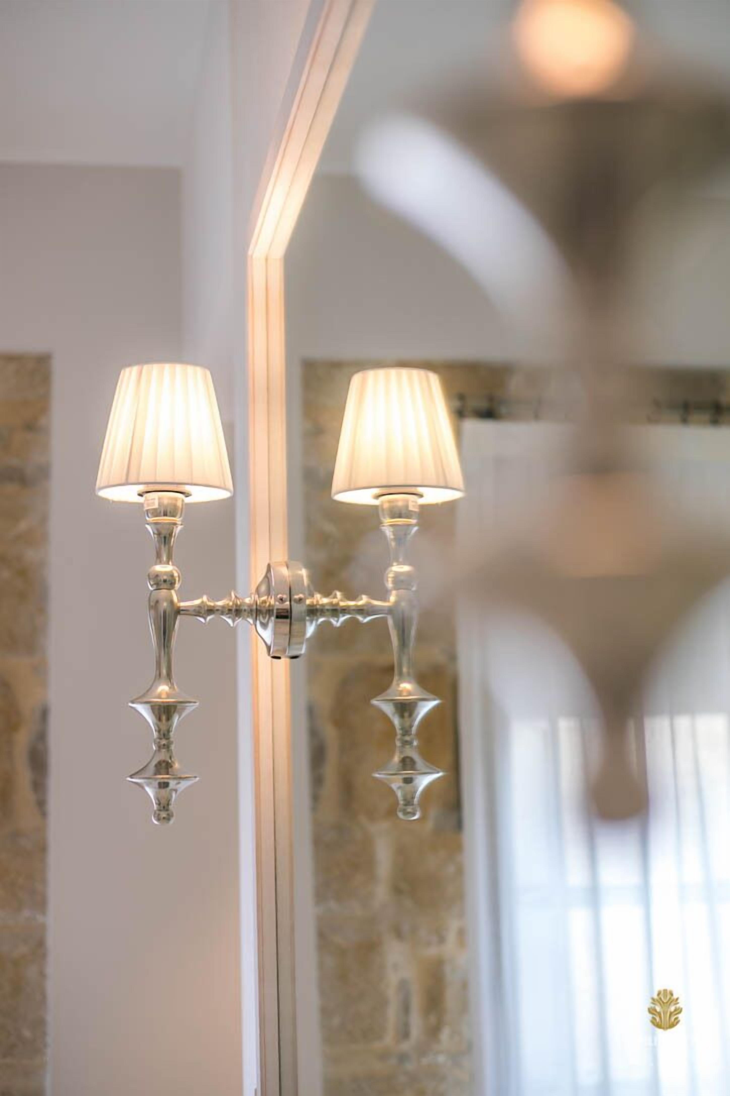 A wall-mounted light fixture with two lamps, a mirror, and a stone wall in the background.