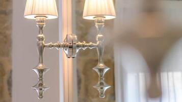 A wall-mounted light fixture with two lamps, a mirror, and a stone wall in the background.
