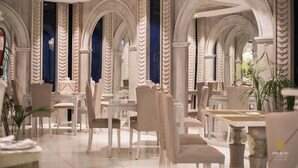 A restaurant with a classic interior featuring arched ceilings and marble columns. Tables and chairs are arranged for dining.